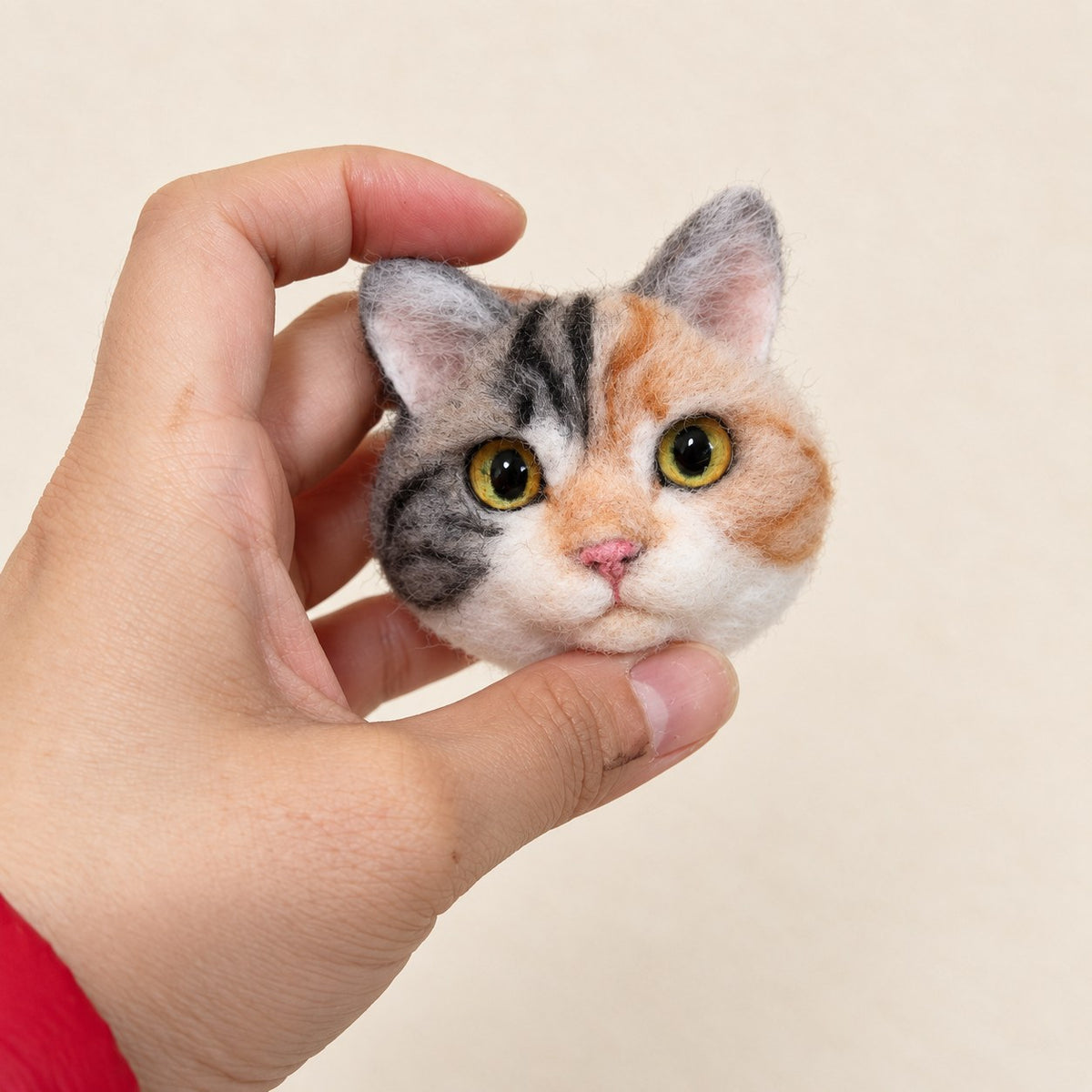 Close-up of a handmade wool-felt orange-and-gray cat charm held in hand