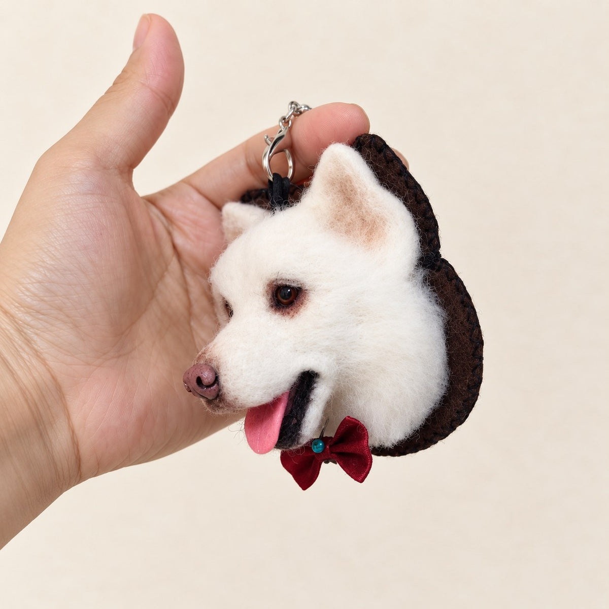 Side view of a handmade wool-felt white dog charm held in hand