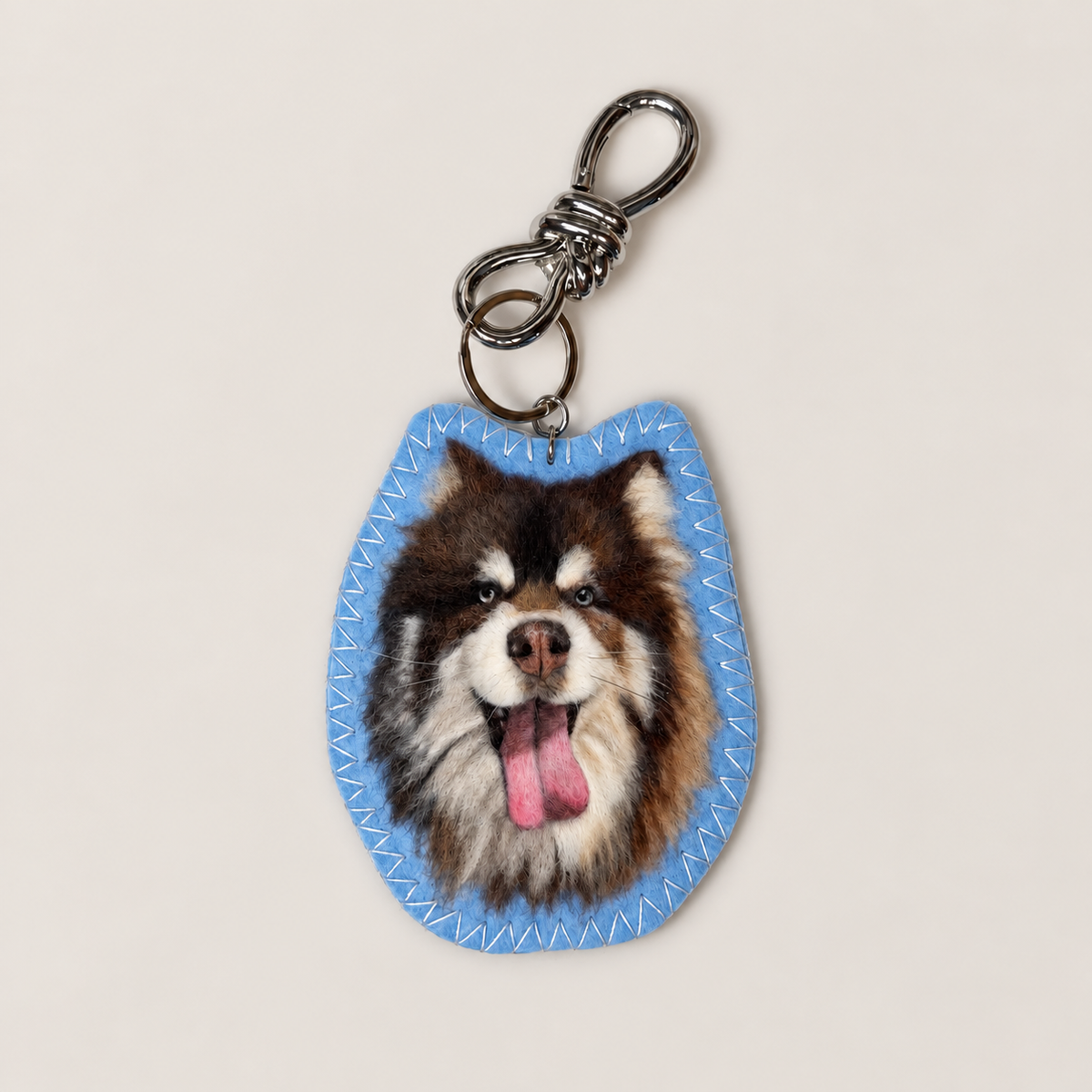 Close-up of a handmade wool-felt brown-and-white dog charm on a clasp